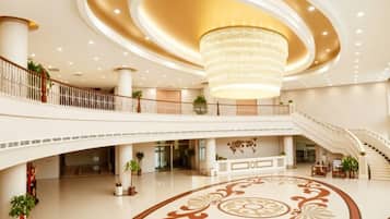 A spacious lobby with a grand chandelier, multiple staircases, and a decorative floor pattern.