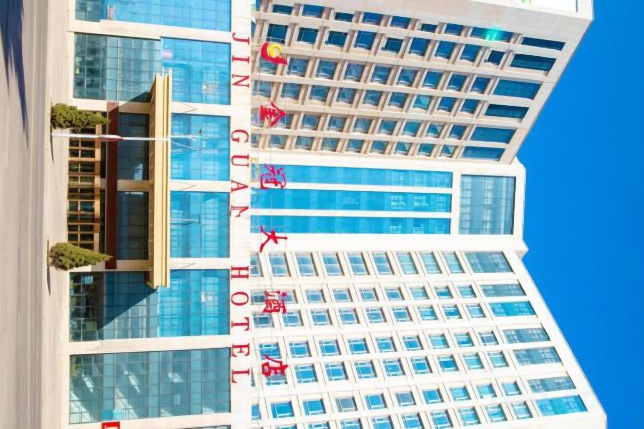 Un immeuble de grande hauteur, doté de nombreux étages, de grandes fenêtres et d’une enseigne bien visible indiquant « HÔTEL JIN GUAN ».