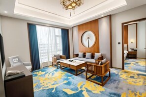 A hotel room with a large bed, a desk with a chair, a sofa, and a coffee table. There is a large window with curtains, a wall clock, and a ceiling light fixture. - Shizuishan Jinguan Hotel (Shizuishan)