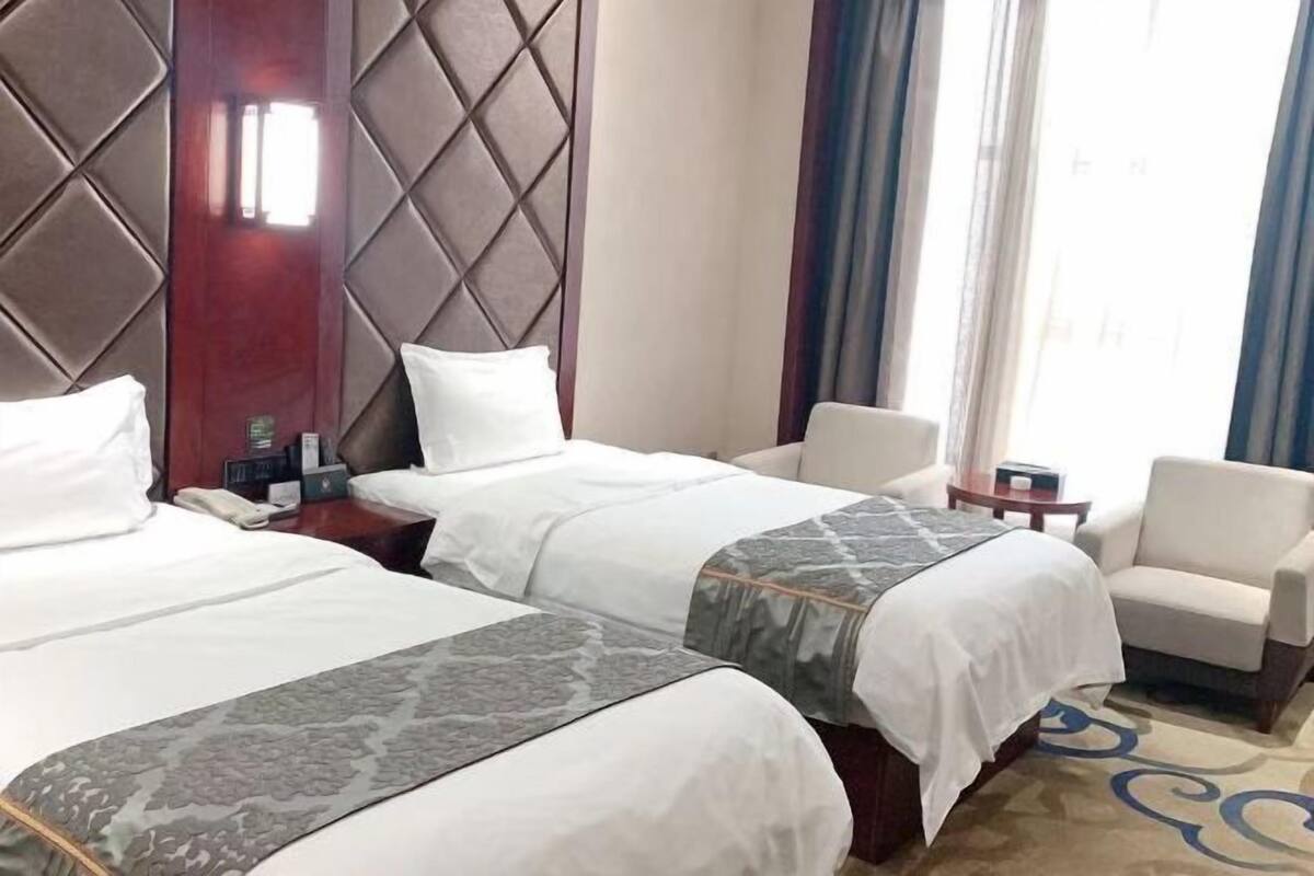 A hotel room with two beds, a sofa, a nightstand, and a window with curtains.