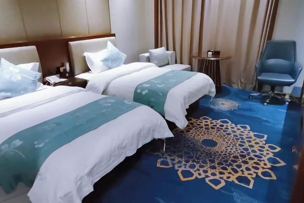 A hotel room with two beds, a blue patterned carpet, a small round table, and a blue chair.
