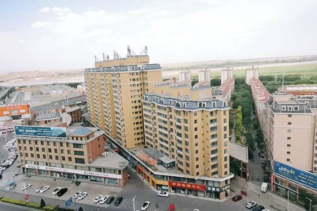 Un edificio alto con varios pisos, rodeado de otros edificios y un estacionamiento.
