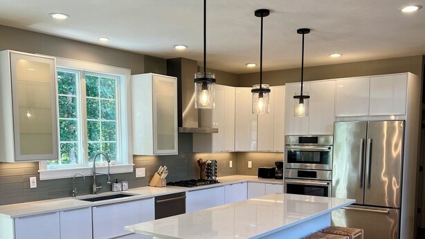 Una cocina moderna con armarios blancos, una isla grande con taburetes de bar, electrodomésticos de acero inoxidable e iluminación colgante.