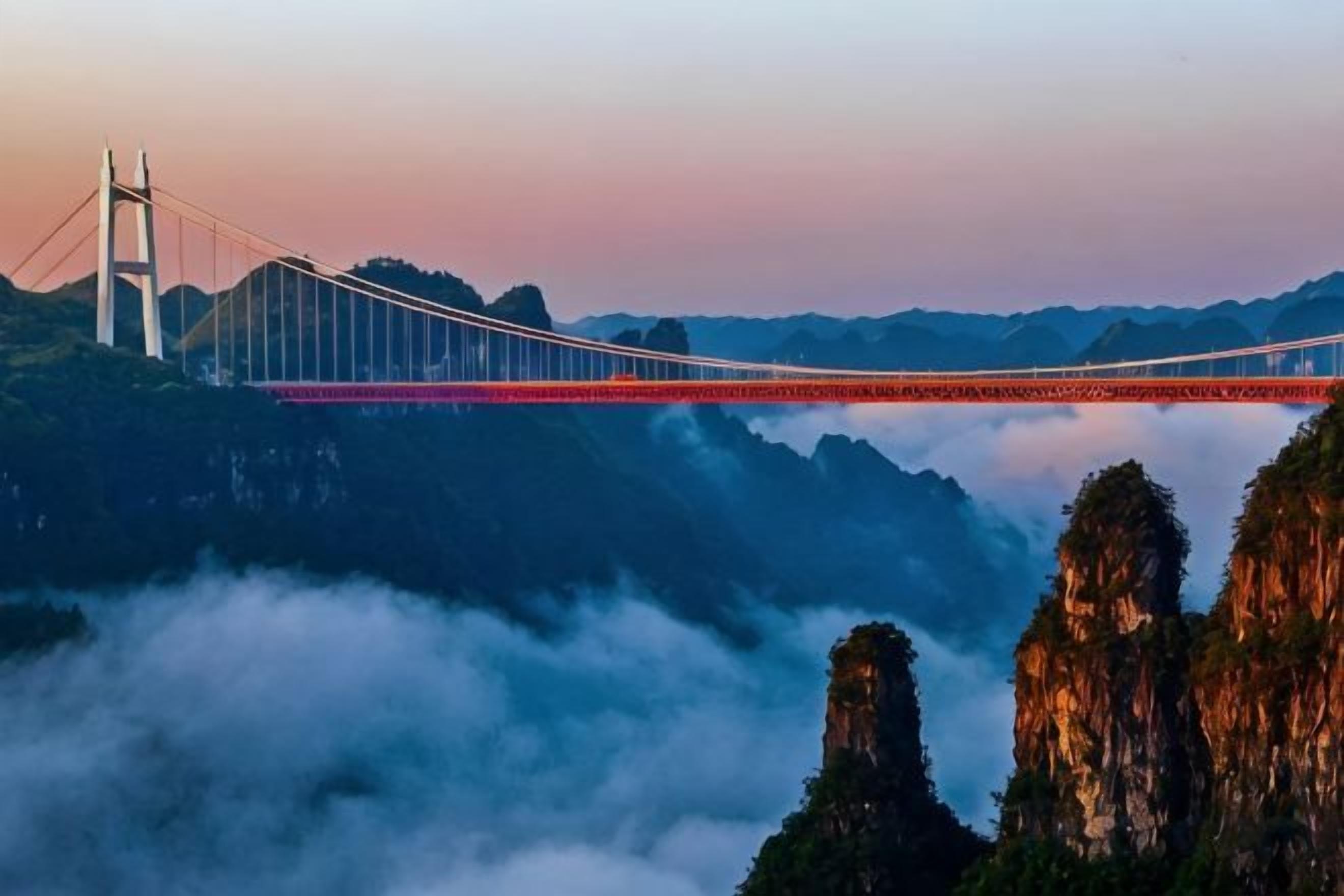 A suspension bridge spanning over a valley with misty mountains in the background.