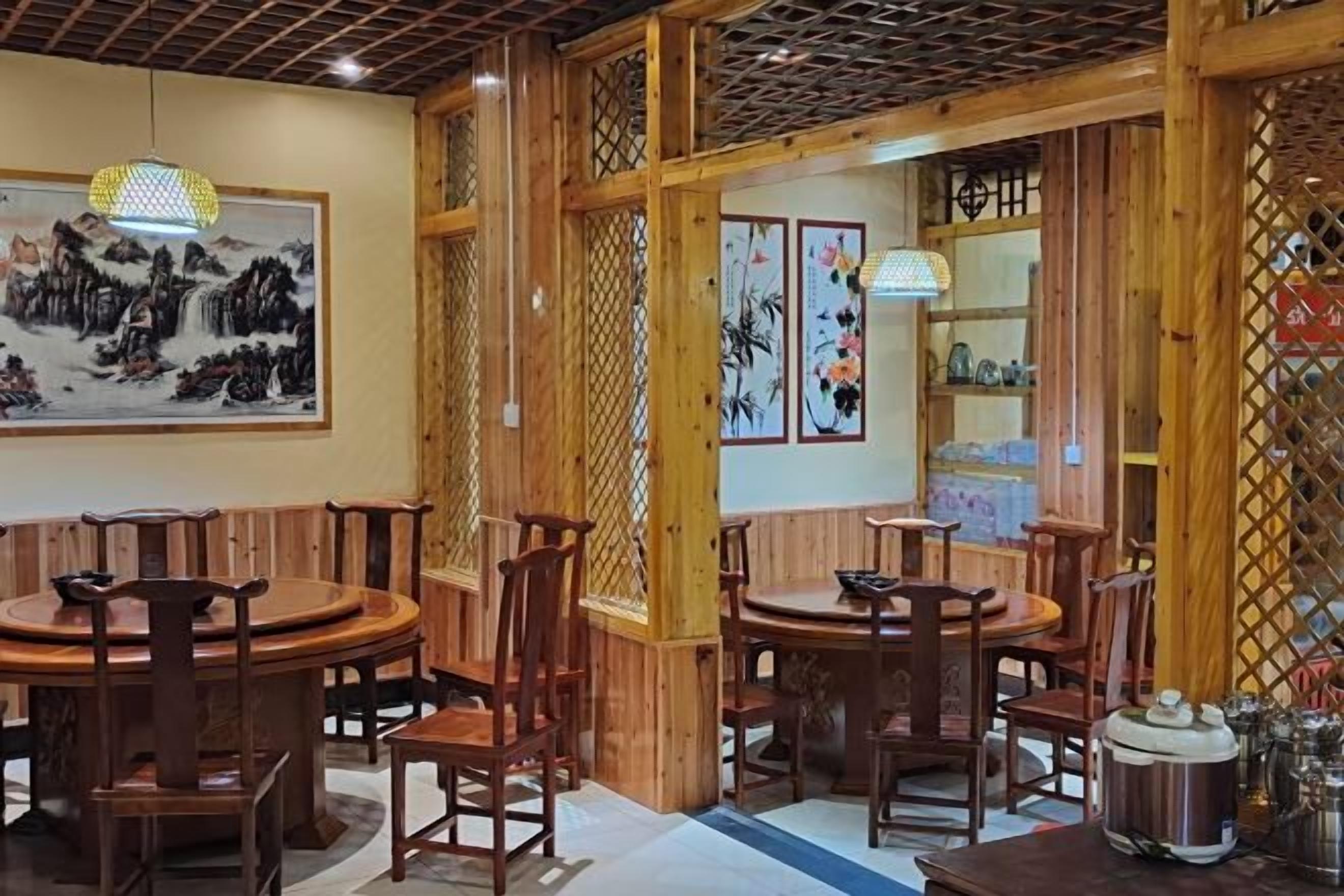 A traditional wooden interior with round tables and chairs, decorative wall art, and a lattice partition.