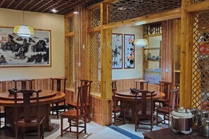 A traditional wooden interior with round tables and chairs, decorative wall art, and a lattice partition. - Jishou Delu Aya Inn (Jishou)