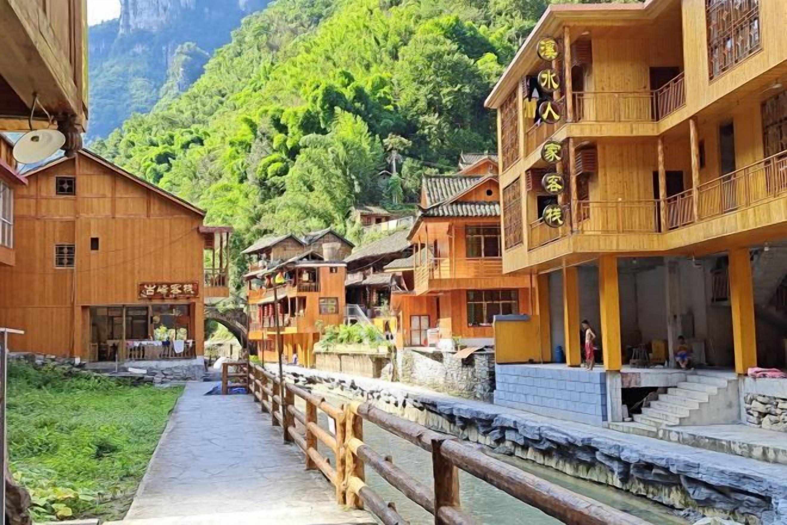 A traditional wooden building with a balcony, a stone pathway, and a river in the background.