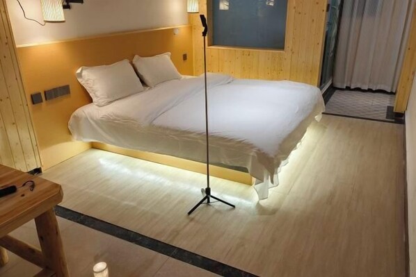 Un lit bien fait, avec une couette blanche et des oreillers, une table de chevet en bois et une lampe sur pied.