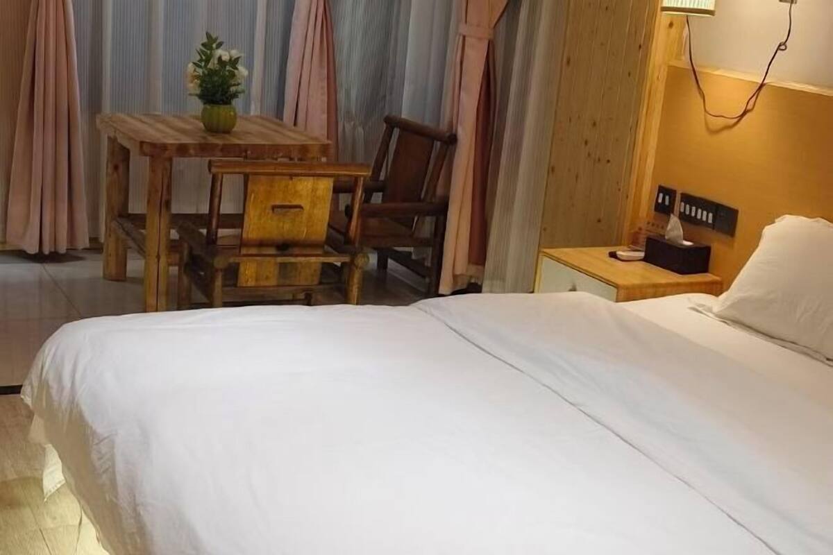 A hotel room with a bed, a wooden table with chairs, a nightstand, and a lamp.