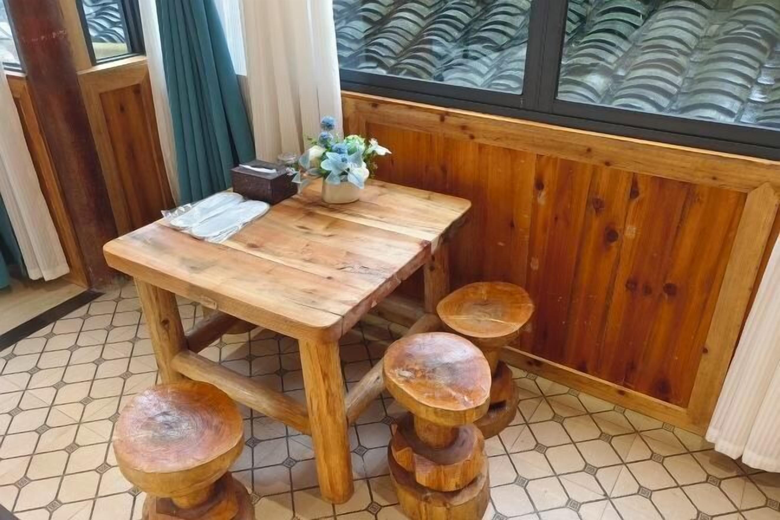 A wooden dining table with a vase of flowers, accompanied by four stools.