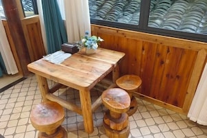 Una mesa de madera para comer con un florero, acompañada de cuatro taburetes.