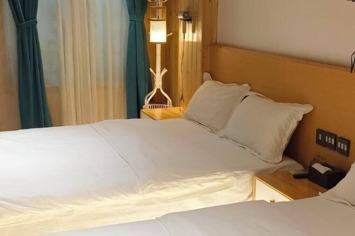 A hotel room with a bed, a nightstand, a lamp, and a window with curtains.