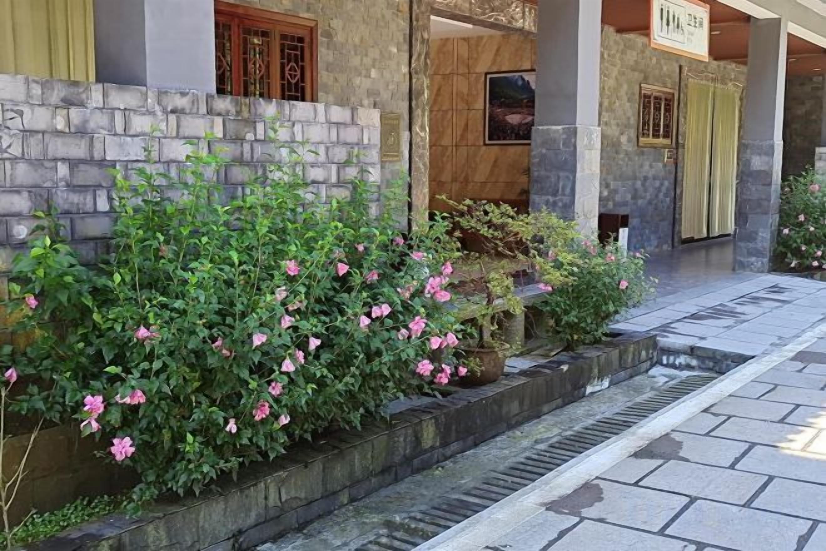 A building entrance with a stone wall, a small water feature, and a sign above the door.