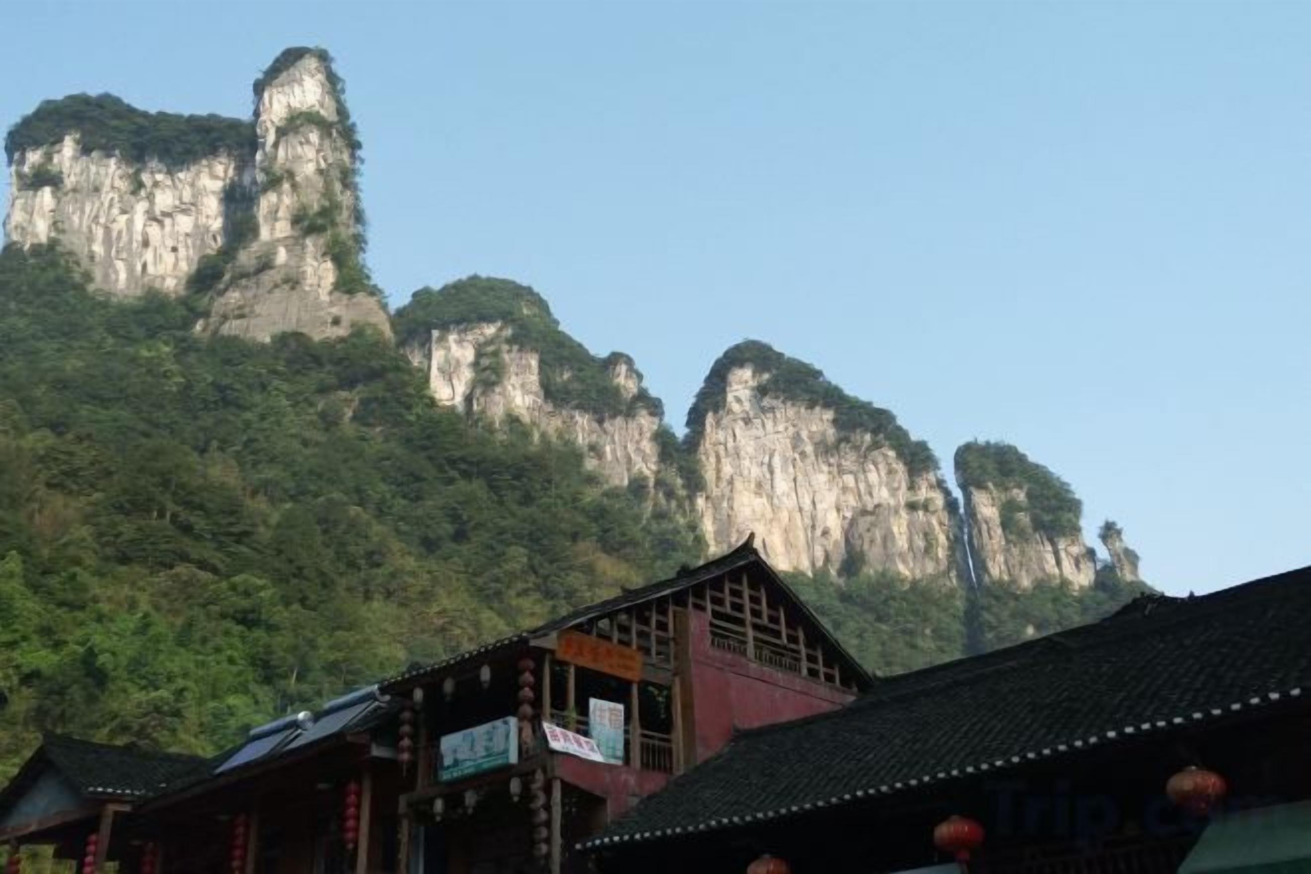 A traditional building with a tiled roof and a balcony, set against a backdrop of a mountainous landscape.