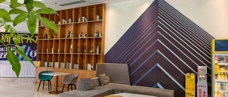 Um lobby moderno com um sofá em seção, uma estante de madeira e um grande painel geométrico na parede.