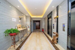 A hotel corridor with a reception desk, a plant, a trash bin, and an elevator. - Chaoman Hotel (Foshan Lingnan Tiandi Pearl Sports Stadium Branch) (Foshan)
