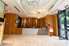 A reception area with a wooden reception desk, a television screen, and a glass door leading outside. - Chaoman Hotel (Foshan Lingnan Tiandi Pearl Sports Stadium Branch) (Foshan)