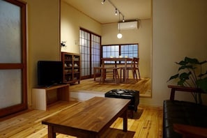 A traditional Japanese-style living room with tatami flooring, a low wooden table, a black leather sofa, a television, and a dining area with a low table and chairs. - Kyoto Station South (Kyoto)