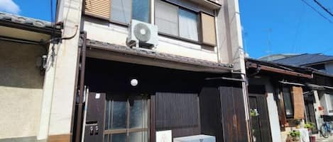 A two-story building with a ground-level entrance, a small air conditioning unit on the roof, and a bicycle parked outside.