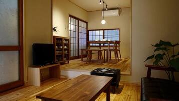 A traditional Japanese-style living room with tatami flooring, a low wooden table, a black leather sofa, and a television.