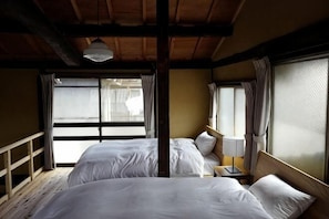 A room with two beds, wooden beams, a window with curtains, and a nightstand with a lamp. - Kyoto Station South (Kyoto)