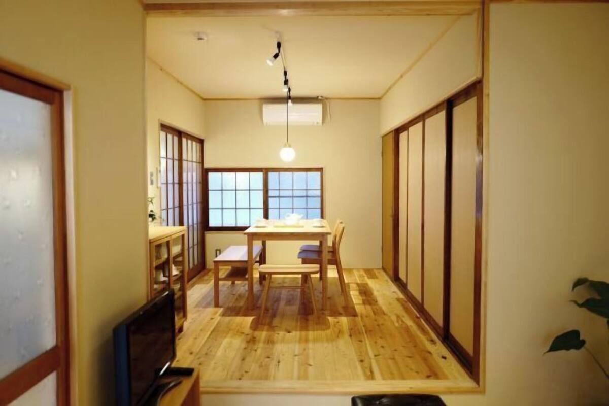 Una habitación japonesa tradicional con suelo de tatami, una mesa baja con cojines, puertas correderas y una lámpara colgante.