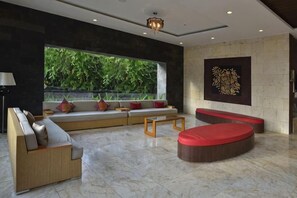 A modern interior with a seating area, a large window, and a decorative wall piece. - Serela Kuta (Bali)