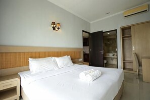 A hotel room with a bed, nightstand, wall-mounted light, and a wardrobe. - Serela Kuta (Bali)