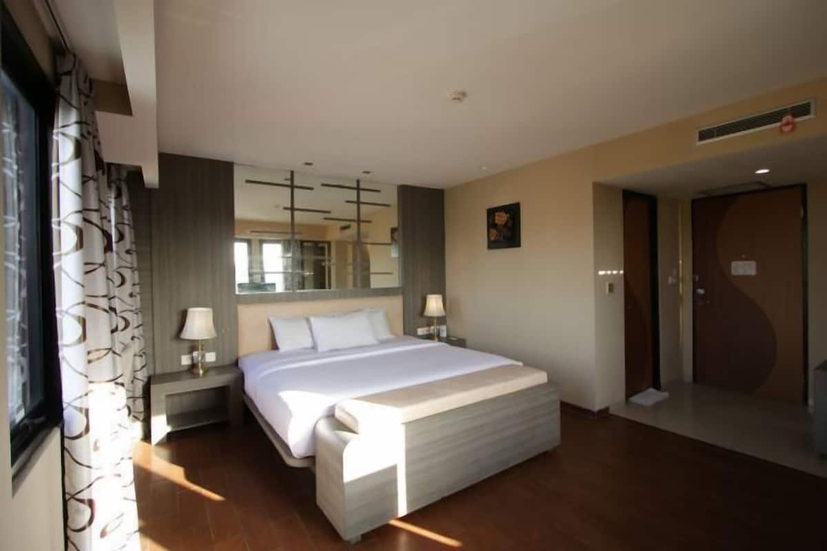 A modern hotel room with a large bed, bedside lamps, a mirror, and a door.