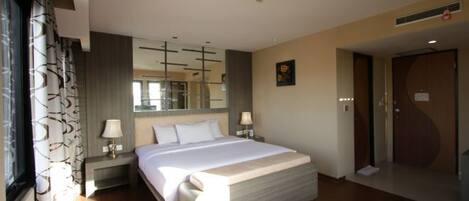 A modern hotel room with a large bed, bedside lamps, a mirror, and a door.
