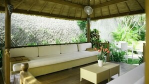 A covered outdoor seating area with a cushioned bench, a small table, and potted plants.