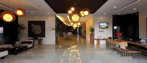 A hotel lobby with a marble floor, seating area, reception desk, and modern lighting fixtures.