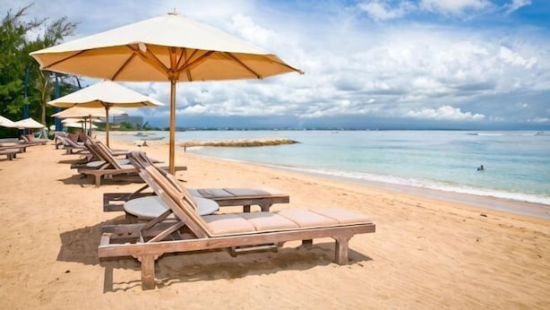 A beach with lounge chairs and umbrellas, a clear sky, and a calm sea.
