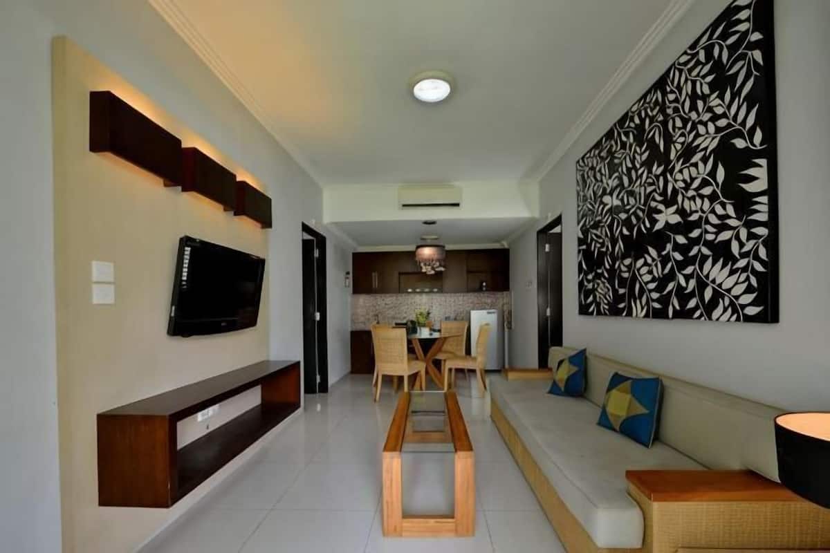 A modern living room with a TV, seating area, and a kitchen in the background.