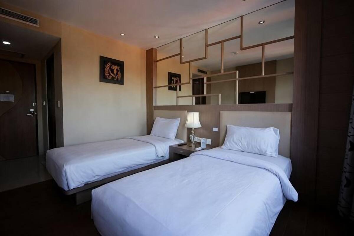 A hotel room with two single beds, a nightstand with a lamp, a mirror, and a door leading to another room.
