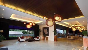 A modern lobby with a seating area, hanging spherical light fixtures, and a large window offering a view of greenery.