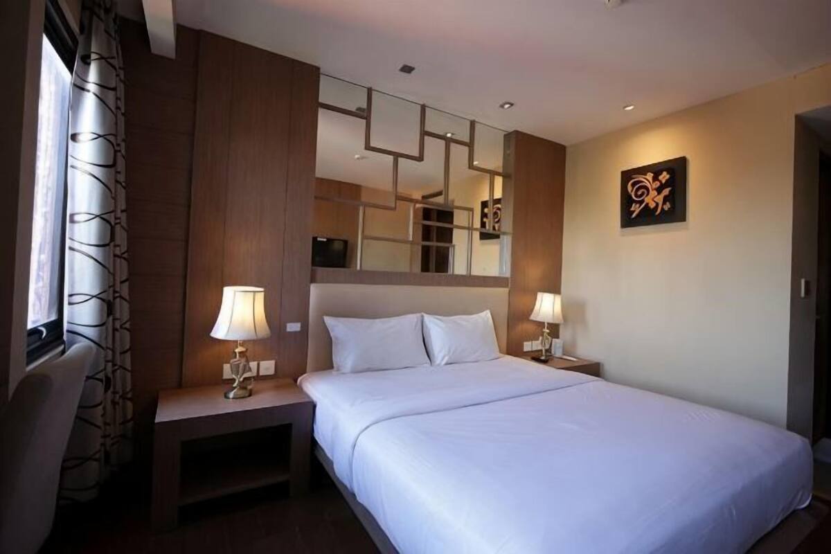 A hotel room with a large bed, two bedside tables with lamps, a mirror, and a wall-mounted artwork.