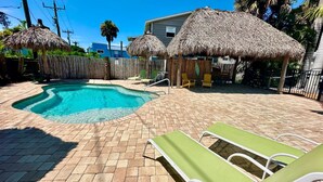 Un jardin avec une piscine, des chaises longues et des parasols en chaume.