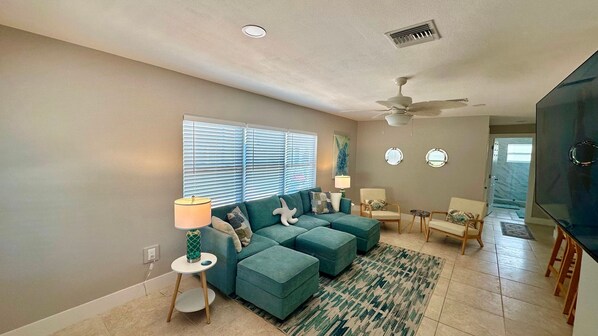 A living room with a sectional sofa, two armchairs, a coffee table, a TV, and a ceiling fan. - Turtle Nest Beach House (Fort Myers Beach)