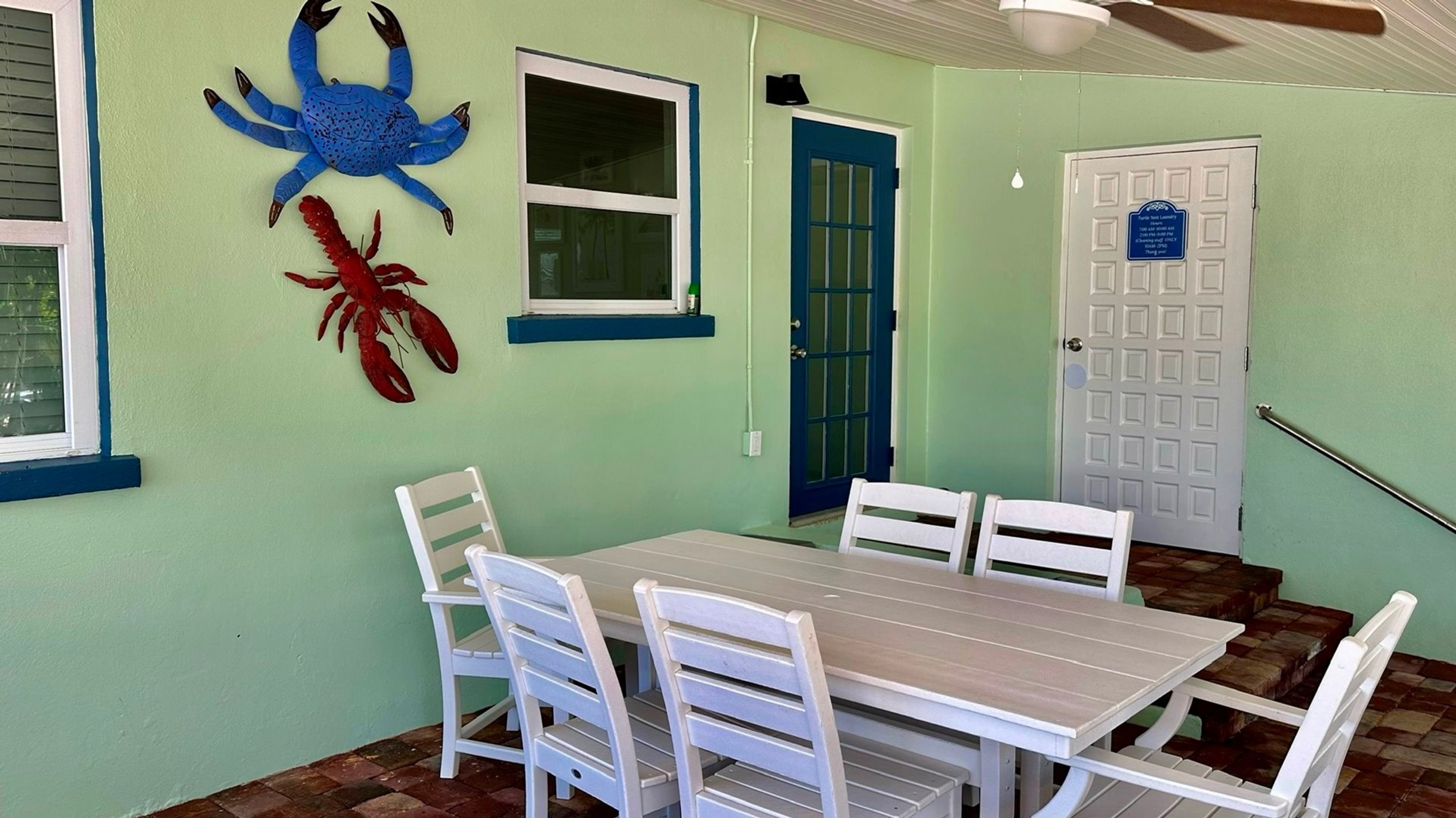 Un coin repas avec une table et des chaises, une décoration représentant un crabe bleu, une décoration représentant un homard rouge et une porte avec une pancarte.