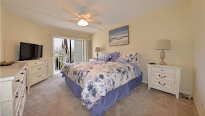 A bedroom with a bed, a television, a ceiling fan, and a view of the outdoors. - Seagrape Bay 205 in Fort Myers Beach (Fort Myers Beach)