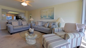 A living room with a sofa, armchair, and ottoman, a glass coffee table, and a ceiling fan. - Seagrape Bay 205 in Fort Myers Beach (Fort Myers Beach)