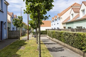 A residential street with houses, a tree-lined sidewalk, and a hedge. - Residence Les Villas De La Baie (Le Crotoy)