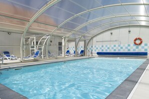 An indoor swimming pool with clear water, blue lounge chairs, and a lifebuoy on the wall. - Residence Les Villas De La Baie (Le Crotoy)