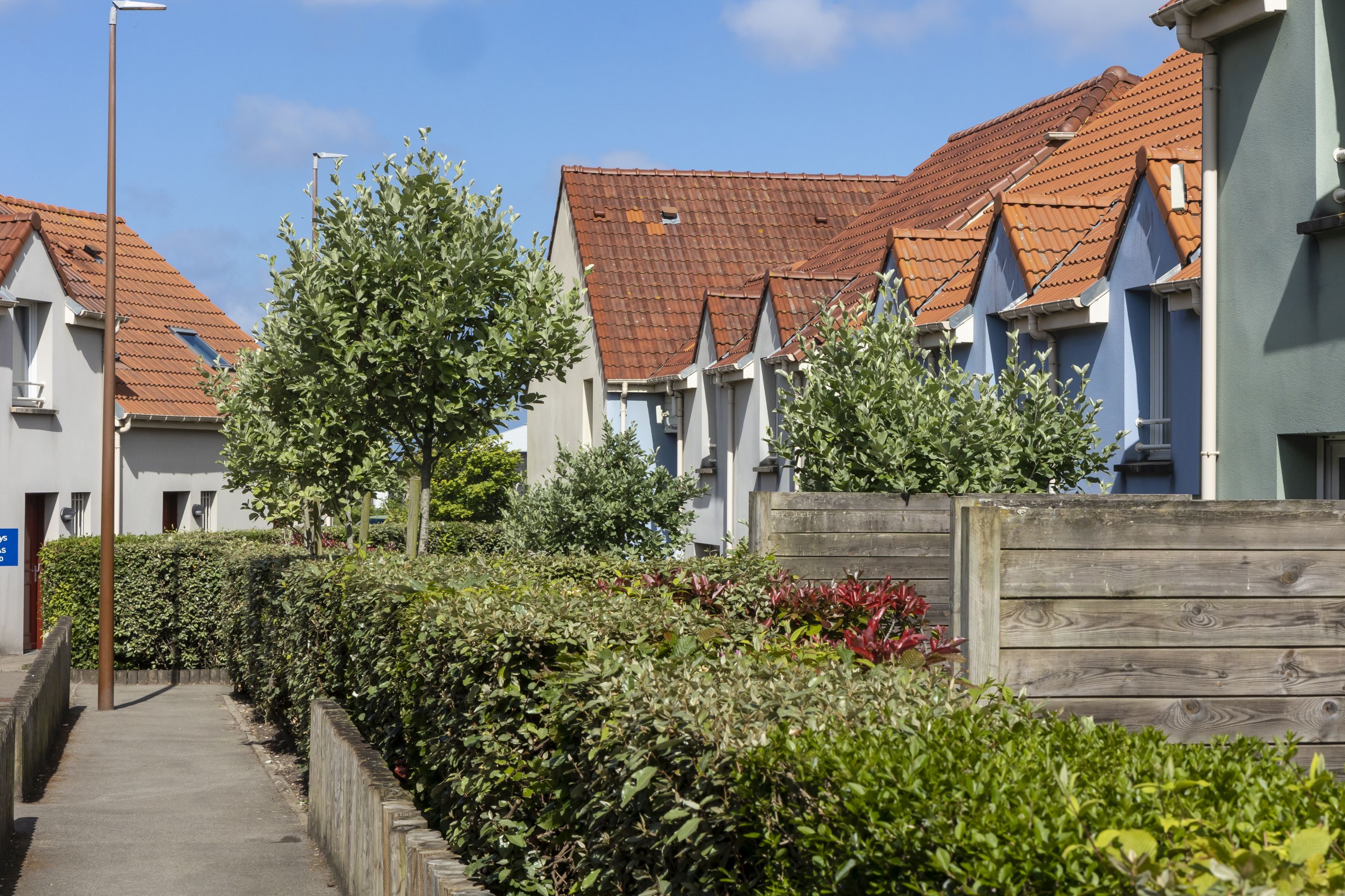 A row of residential buildings with red-tiled roofs and white walls, a wooden fence, and a clear sky.