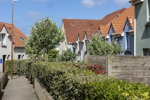 Une rangée d’immeubles résidentiels aux toits recouverts de tuiles rouges et aux murs blancs, une clôture en bois et un ciel dégagé.