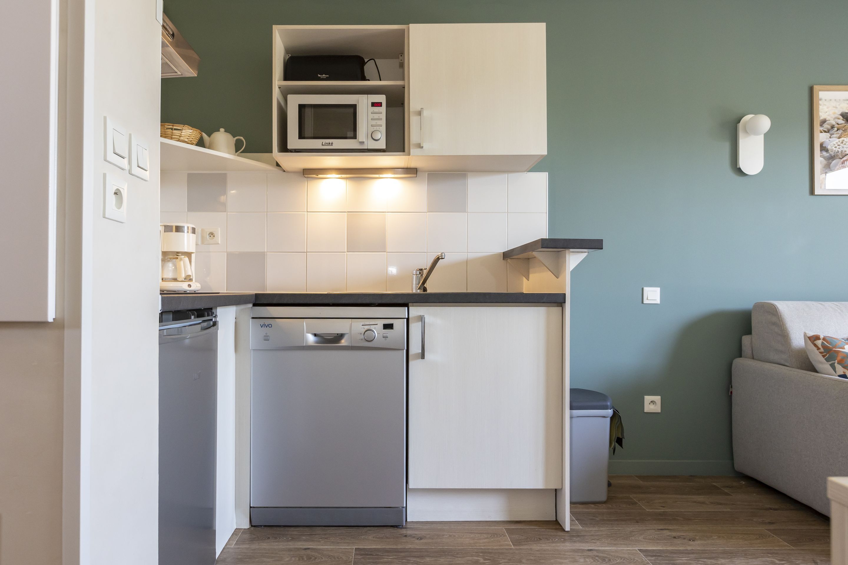 A compact kitchen with a dishwasher, microwave, and white cabinets.