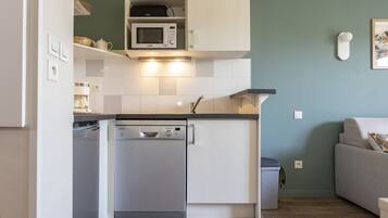 A compact kitchen with a dishwasher, microwave, and white cabinets.