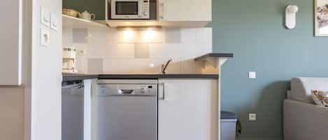 Una cocina compacta con lavavajillas, microondas y armarios blancos.