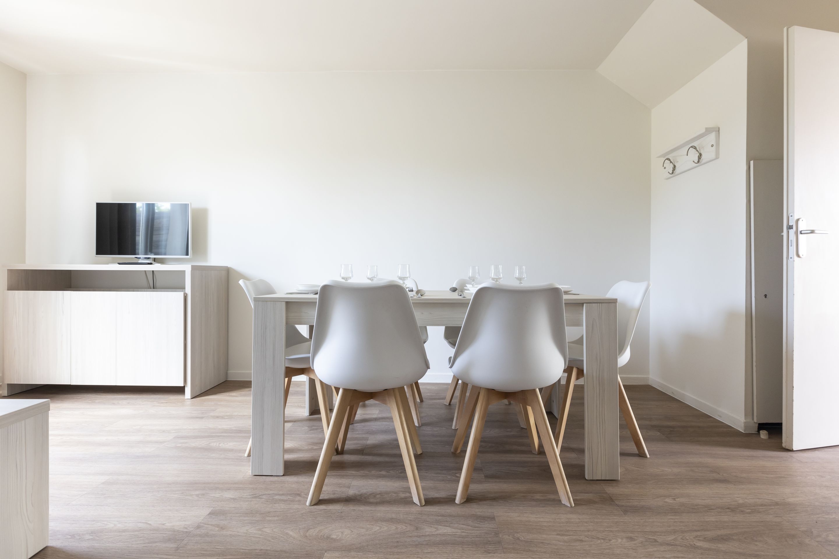 A modern dining area with a white table, four chairs, and a television on a stand.